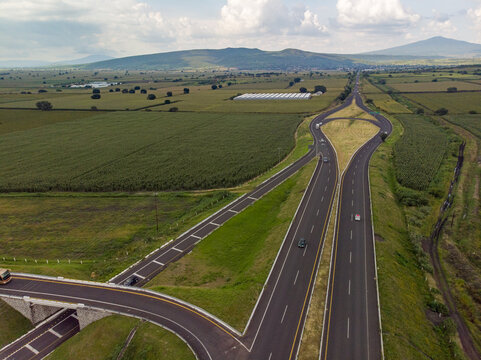 Aerial view of the Autopista Mexico - Guadalajara highway interchange surrounded by lush agricultural fields and green landscape under a cloudy sky in Ecuandureo, Michoacan, Mexico.
