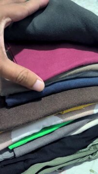 Vertical close-up of a hand flipping through a neat stack of folded colorful t-shirts and clothing