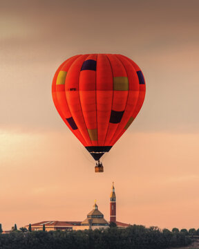 Aerial view of a colorful hot air balloon floating above a church with a tall bell tower at sunset in Corridonia, Marche, Italy.