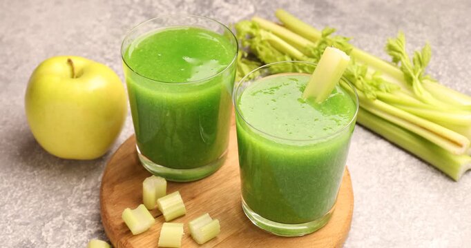 Woman putting celery into glasses with fresh juice at grey table, closeup