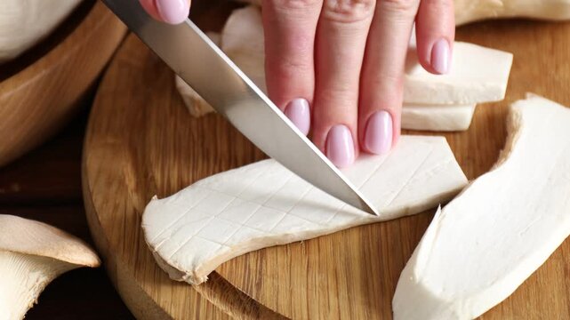 Woman cutting fresh oyster mushroom at table, closeup
