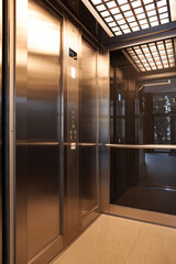Modern polished stainless steel elevator cabin featuring illuminated ceiling and control panel © Jelena