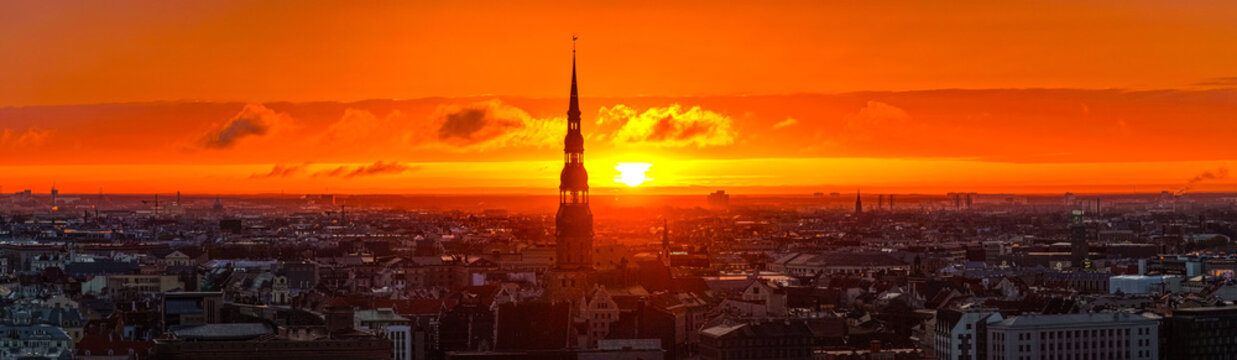 Aerial view of St. Peter's Church spire rising above the historic rooftops of Riga at sunset, Riga, Latvia.