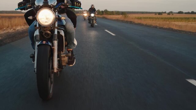 Group of motorcyclists riding on asphalt road during golden hour trip.