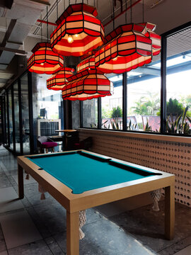 Cozy lounge area showcasing a green felt billiards table and unique vintage-style red lampshades next to bright windows