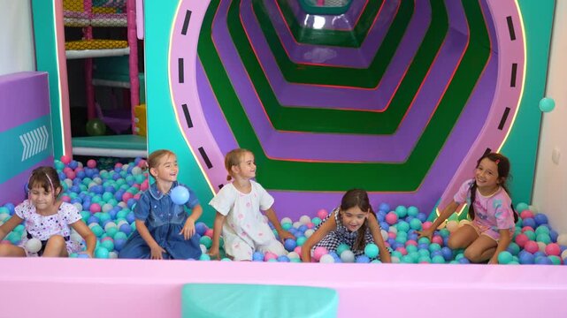 Five smiling girls having fun together, playing and throwing plastic balls in a vibrant dry pool