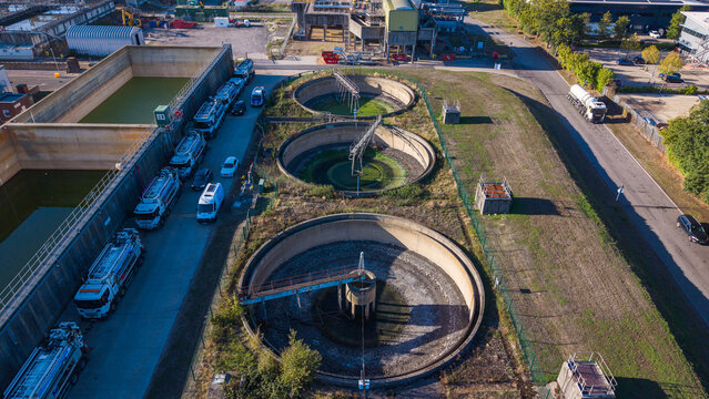 Aerial view of the sewage works in Camberley, showing circular sedimentation tanks, industrial infrastructure, and a line of tanker trucks parked nearby in Camberley, England, United Kingdom.