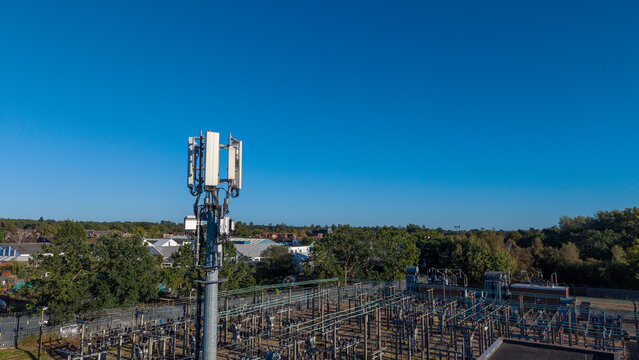Aerial view of a phone mast standing above an electrical substation with surrounding trees and suburban buildings in Camberley, England, United Kingdom.