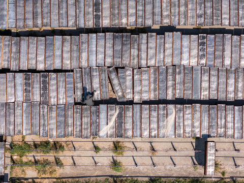 Aerial view of a worker tending to rows of drying noodles on racks in an agricultural field in Polanharjo, Central Java, Indonesia.