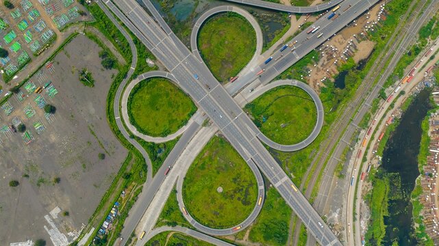 Aerial view of the JNPT Interchange featuring complex cloverleaf ramps, surrounding green spaces, and nearby industrial storage areas in Navi Mumbai, Maharashtra, India.