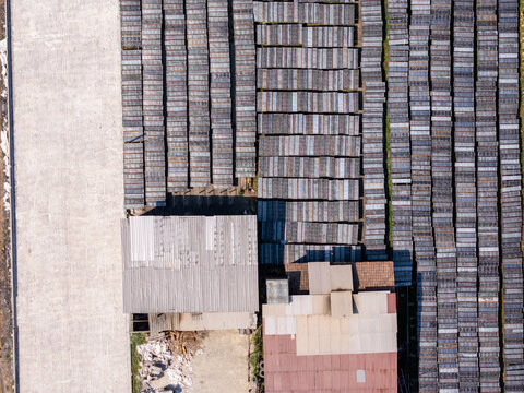Aerial view of an industrial facility with rows of rectangular drying frames in a grid pattern next to a building with a metal roof in Polanharjo, Central Java, Indonesia.