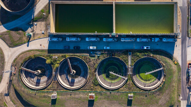 Aerial view of the Water Treatment Centre featuring circular sedimentation tanks, rectangular treatment basins, and service vehicles parked in the facility, Camberley, England, United Kingdom.