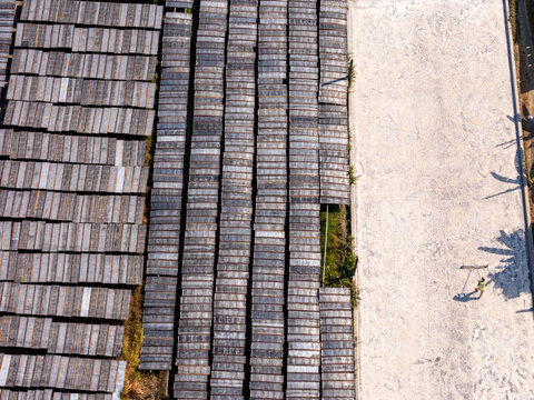 Aerial view of a worker raking a large light-colored drying area beside rows of dark wooden frames, Polanharjo, Central Java, Indonesia.
