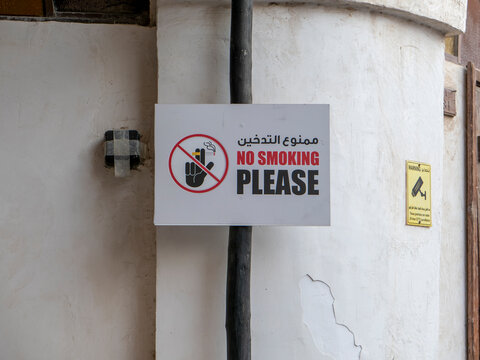 Bilingual no smoking sign in Arabic and English mounted on a pole against a textured plaster wall in Souq Waqif.