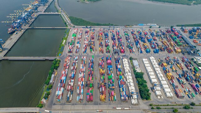 Aerial view of Jawaharlal Nehru Port Authority featuring rows of colorful shipping containers, industrial cranes, and port infrastructure in Juna Sheva, Maharashtra, India.