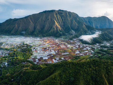 Aerial view of the Sembalun agricultural basin nestled at the foothills of Mount Rinjani with colorful patchwork fields and lush green slopes in Sembalun, West Nusa Tenggara, Indonesia.