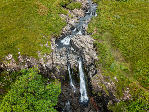 Aerial view of Eas Fors waterfall on the Isle of Mull, Scotland, water flowing over dark rocky ledges into a gorge surrounded by grassy hillsides