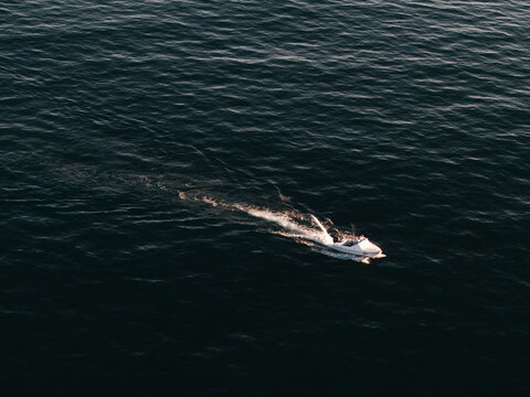 Aerial view of a small white motorboat cruising through the dark blue ocean, leaving a white wake behind it in Dee Why, New South Wales, Australia.