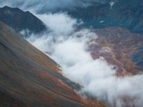 Aerial view of Denali Highway with autumn foliage and mist clinging to the rocky mountain slopes in Cantwell, Alaska, United States.