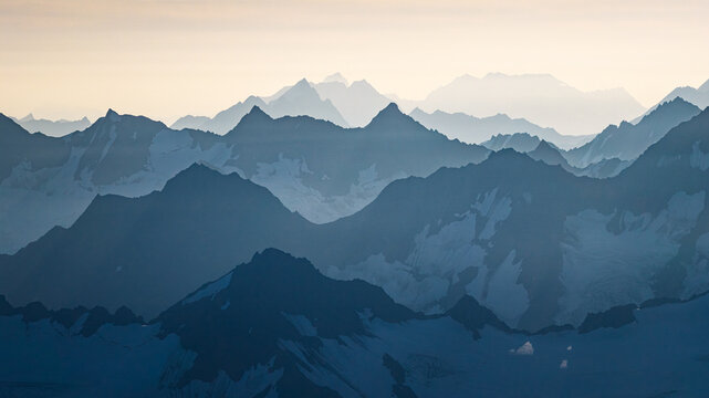 Aerial view of the snow-capped peaks of Chugach State Park with layered mountain ranges fading into the hazy distance in Anchorage, Alaska, United States.