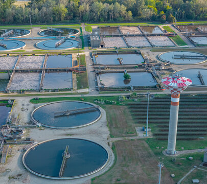 Aerial view of circular clarifiers, aeration basins and a water tower forming part of a large wastewater treatment complex in Italy.