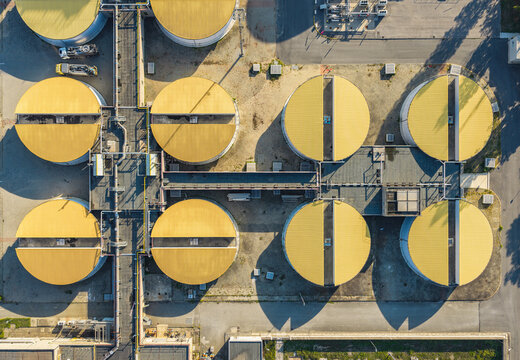 Aerial view of circular wastewater treatment tanks with yellow covers forming a geometric industrial pattern at a facility in Italy.