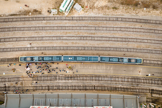 Aerial view of a train stopped at a station platform with passengers waiting, surrounded by multiple railway tracks and the roof of a station building in Buzet, Istria County, Croatia.