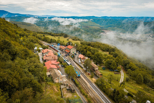 Aerial view of the train station in Buzet surrounded by lush green hills, dense forests, and patches of morning fog in Buzet, Istria County, Croatia.