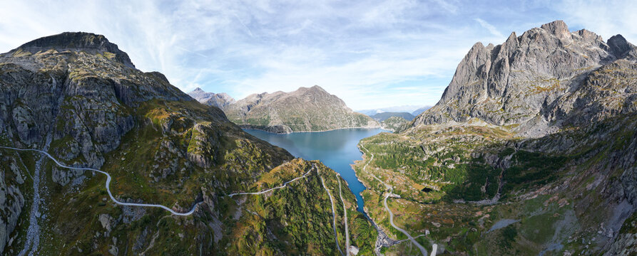 Aerial view of Barrage d'Emosson surrounded by rugged alpine mountains, winding mountain roads, and deep blue water in Finhaut, Valais, Switzerland.