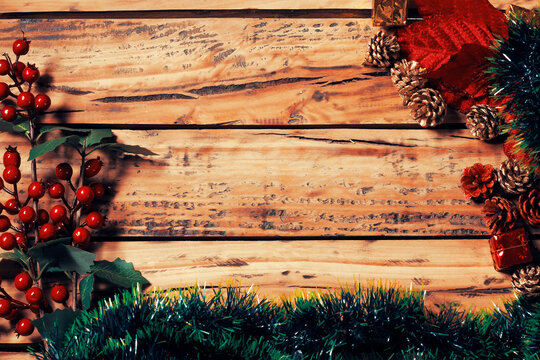 Christmas background on a rustic wooden table with green tinsel, decorative leaves, and gold pinecones, featuring ample space for text.