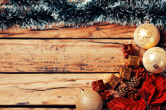 Rustic Christmas background featuring tinsel, gold ornaments, gifts, and pinecones, framed on a wooden table with space for text.