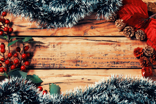 Festive Christmas background on an aged wooden surface framed by decorative branches, pine cones, and small gifts, with space for text.