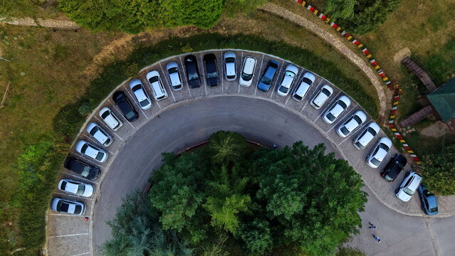 Aerial view of the curved parking lot at Brzece Sports Centar with parked cars surrounded by lush green trees in Brzece, Rasina District, Serbia.