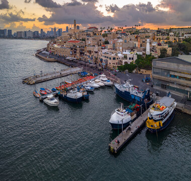 Aerial view of the historic Old port of Jaffa with fishing boats docked at the pier, stone buildings, and the Tel Aviv skyline in Tel Aviv-Yafo, Tel Aviv District, Israel.
