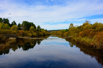 Fototapeta premium Broad tranquil river mirrors dramatic cloudy sky and golden‑hued woodland, rolling forested hills stretch into distance in northern China wilderness.