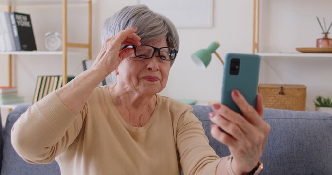 Senior woman with glasses squints, smartphone vision problem. She peers close, adjusting focus eyesight, myopia, hyperopia, presbyopia make reading hard. Key theme age-related vision challenge.