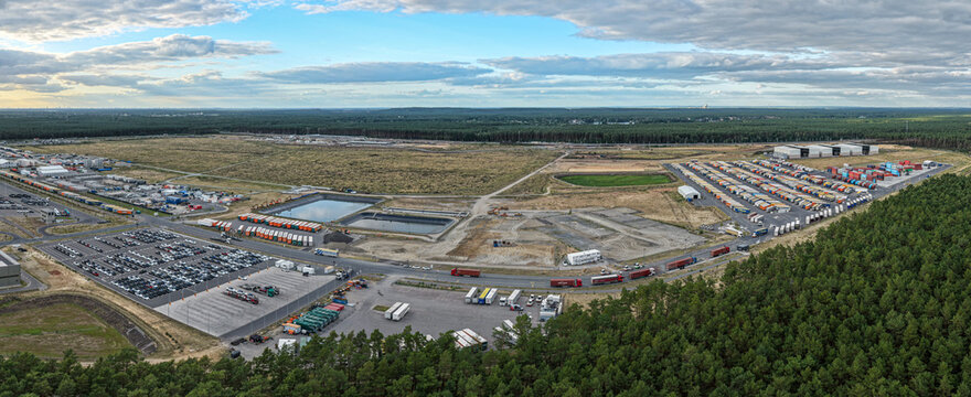 Aerial view of the Tesla Gigafactory Berlin-Brandenburg site featuring large parking lots, industrial logistics areas, and surrounding forest in Grunheide Mark, Brandenburg, Germany.