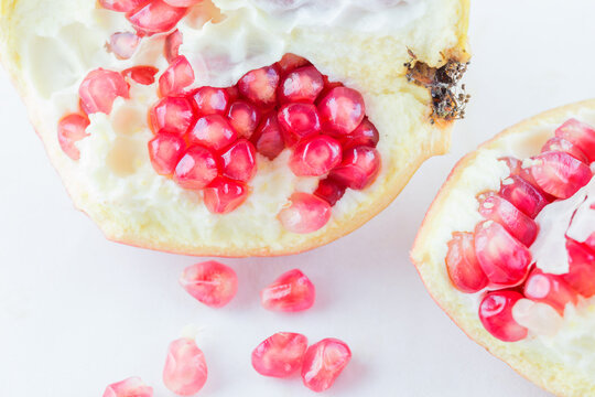 Close-up of sliced fresh pomegranate with bright red arils and scattered seeds on a plain white surface.