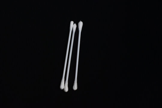 Three white cotton buds isolated on a solid black background, concept of hygiene and personal care