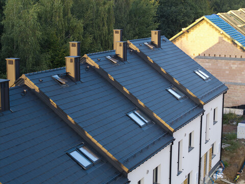 Aerial view of modern residential houses with dark tiled roofs, chimneys, and skylights in Poland.