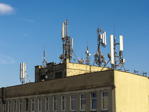 Aerial view of telecommunication towers and antennas mounted on a building rooftop against a clear blue sky in Poland.