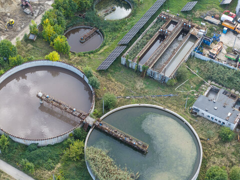 Aerial view of a wastewater treatment plant featuring large circular sedimentation tanks, rectangular aeration basins, and solar panels in Poland.