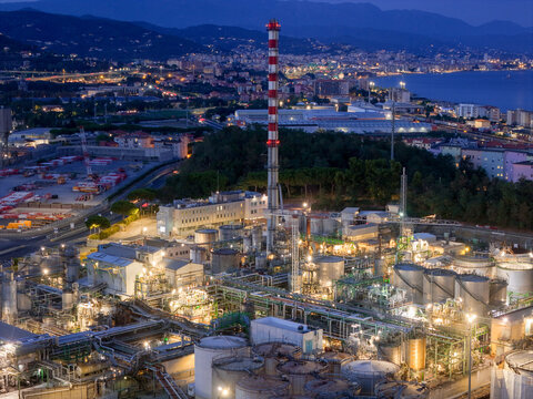 Aerial view of the plant for the production of finished lubricants illuminated at night with industrial tanks, piping, and a tall chimney in Vado Ligure, Liguria, Italy.