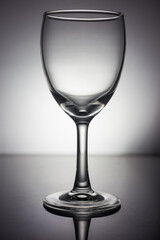 Obraz premium A clean, empty transparent wine glass placed on a smooth reflective surface in a studio setting, captured in monochrome tones.