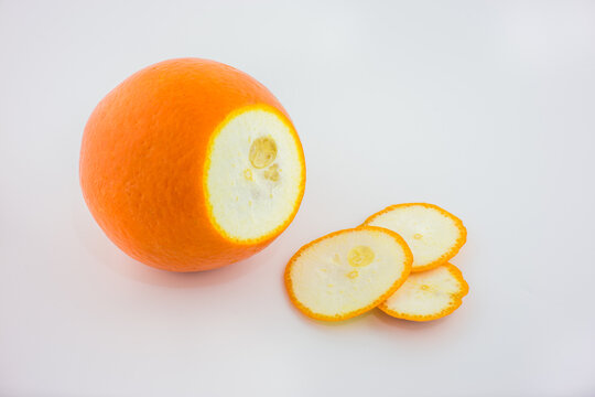 A whole orange and three sliced pieces displayed on a plain white background, showing their pith and seeds.
