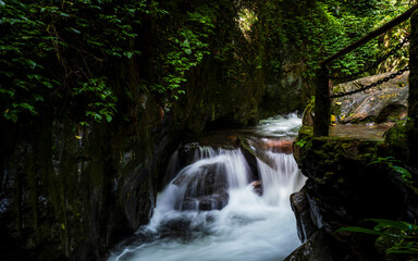 Fototapeta premium Slow motion stream among wet rocks in Shimen Gorge, Ailao Mountain, Yuxi, Yunnan, China. Forest creek flowing over mossy stones, long exposure photography.