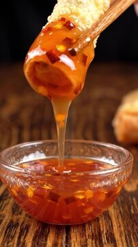 Wooden chopsticks dipping a golden crispy spring roll into a small bowl of sweet chili sauce