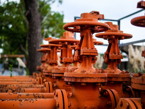 Industrial valve material: close-up of orange-red pipes and handwheel, heavy industrial style photography, abandoned old-era vibe