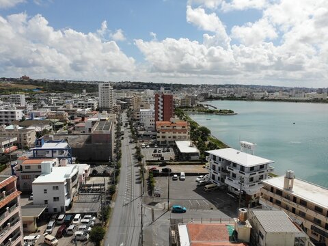 Aerial view of Arah Beach featuring a coastal promenade, emerald-green sea, and urban buildings under a cloudy sky in Chatan, Okinawa, Japan.