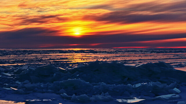 Aerial view of a frozen sea with jagged ice floes under a vibrant sunset sky in Latvia.